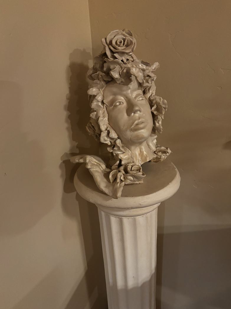 White ceramic bust of a face crowned with sculpted roses on a column pedestal