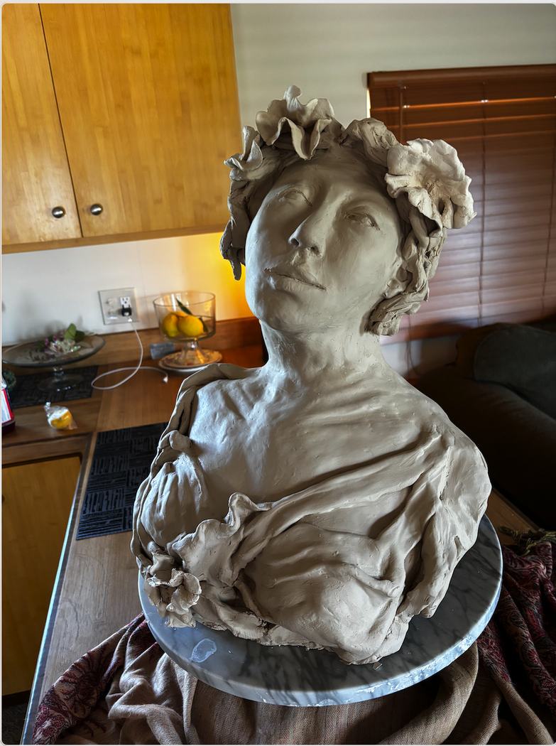 Unfired clay bust of a woman with a floral crown and draped shoulders in the studio