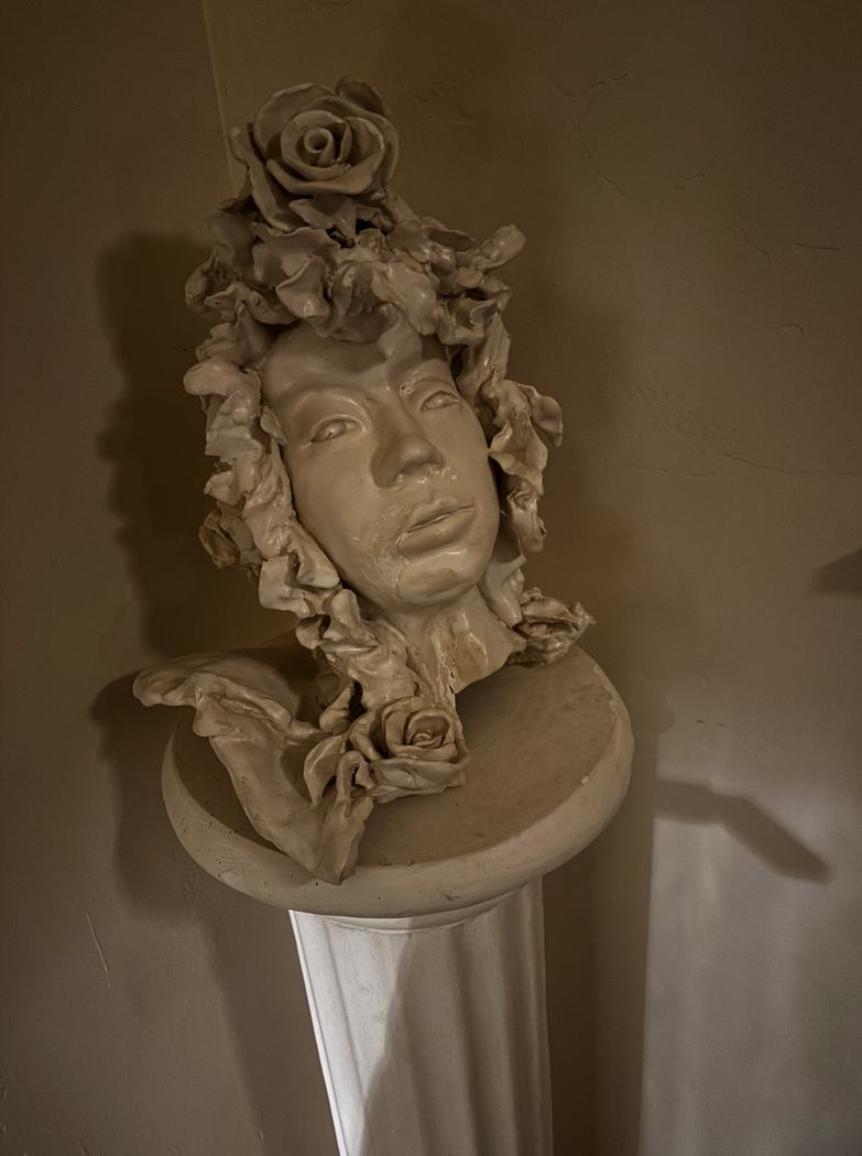 Close view of a ceramic bust framed by sculpted roses and ribbons